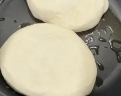 Step <p>6. Aplaste ligeramente las bolas con la mano y cocine los panes en una sartén antiadherente a baja temperatura (para que se desarrollen) durante 6-8 minutos por cada lado. Retire de la sartén y deje templar unos minutos.</p> illustration