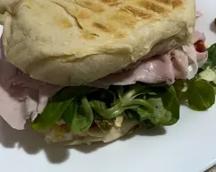 Step <p>7. Corte el pan por la mitad horizontalmente. Ponga sobre una mitad 1 hoja de lechuga, 1 cucharada de ensalada de huevo, 2-3 láminas de pepinillo y 1-2 lonchas de jamón cocido. Tape con la otra mitad. Repita el proceso con los panes restantes y sirva.</p> illustration