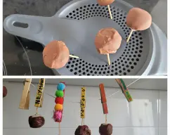 Step <p>Sumerge las bolitas en el chocolate derretido y déjalas enfriar colocando cada palito sujeto en una pinza de la ropa, en los agujeros de la tapa antisalpicaduras, en algún corcho o colgados en pinzas<br></p> illustration